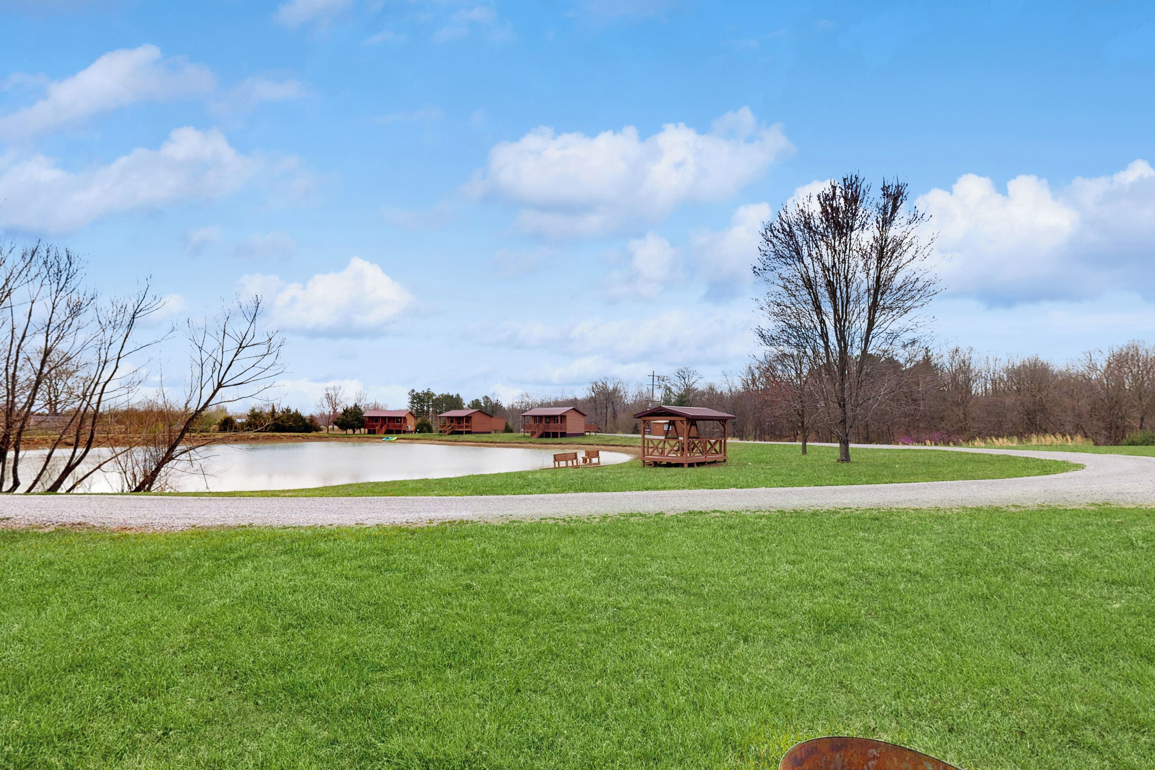 A park with a pond, picnic tables, and wooden structures.