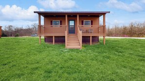 A two-story wooden cabin with a balcony, a front door, and a staircase leading to the entrance. - Pet Friendly! Couples Retreat in Southern Illinois (Murphysboro)