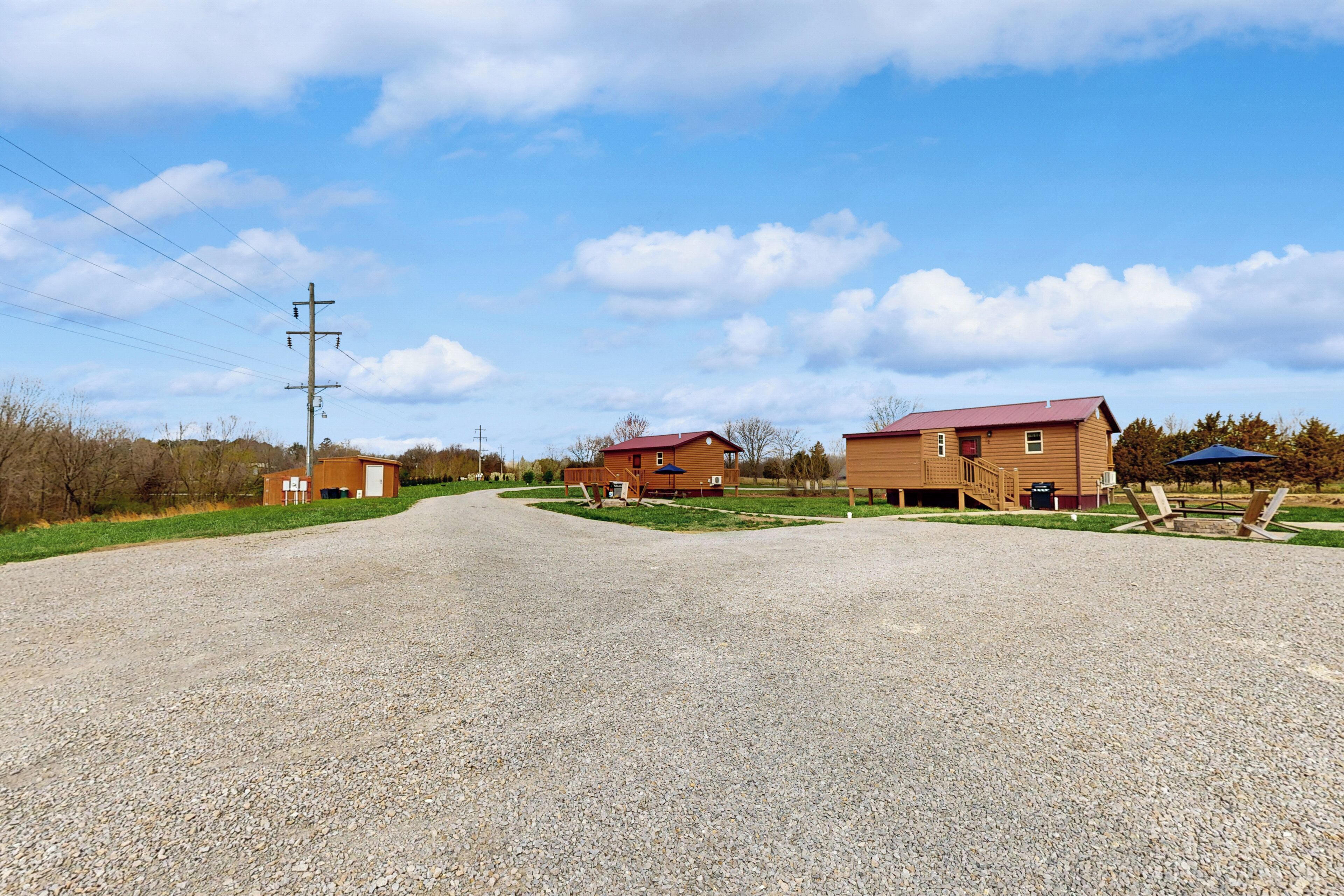 A gravel driveway leading to a wooden house with a red roof, a small shed, and a utility pole.