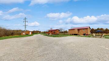 A gravel driveway leading to a wooden house with a red roof, a small shed, and a utility pole.