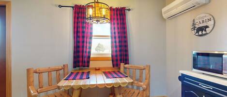 A wooden dining table with a checkered tablecloth, surrounded by wooden chairs. An air conditioning unit is mounted on the wall above the table.