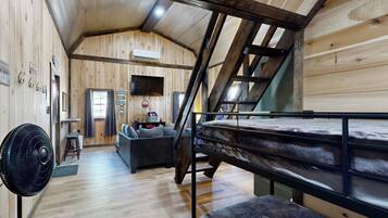 A wooden cabin interior with a bunk bed, a fan, a sofa, and a staircase.