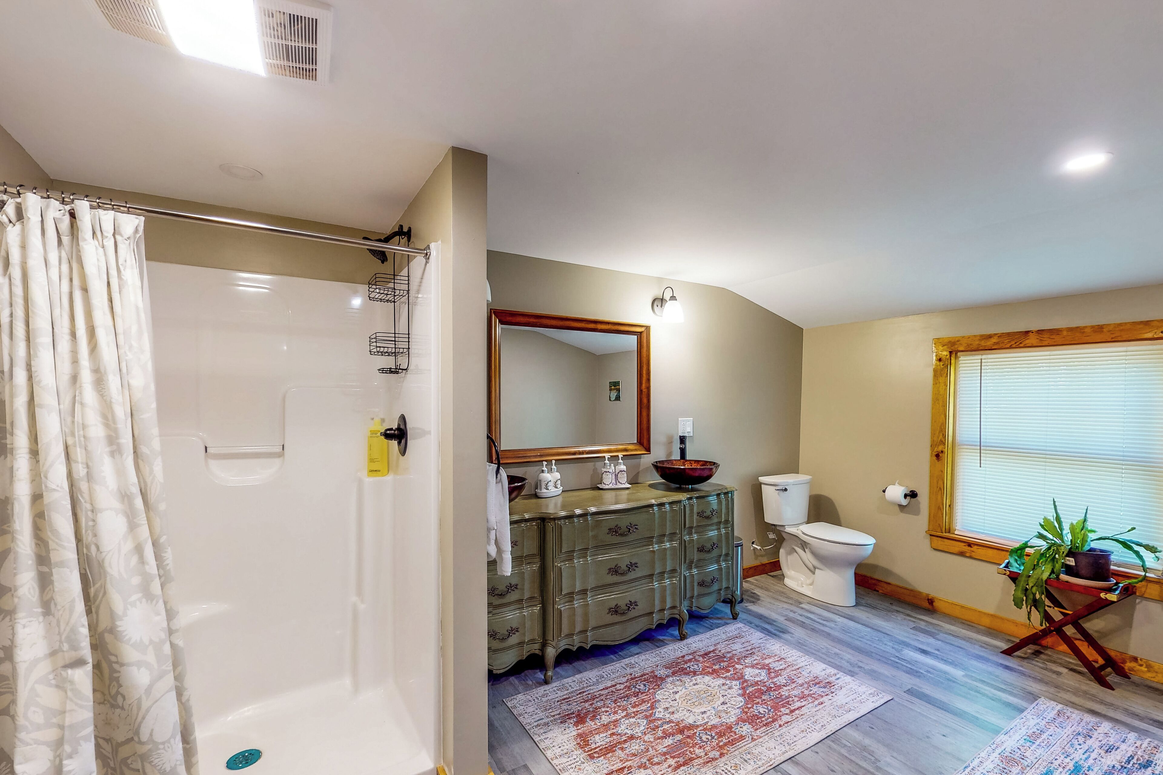 A bathroom with a shower, toilet, vanity, and a large mirror.