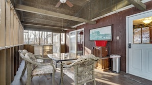 A covered outdoor area with wicker furniture, a glass table, and a door with a view of a snowy landscape. - Roaring Spring Horse Farm Getaway w/ Game Room (Roaring Spring)