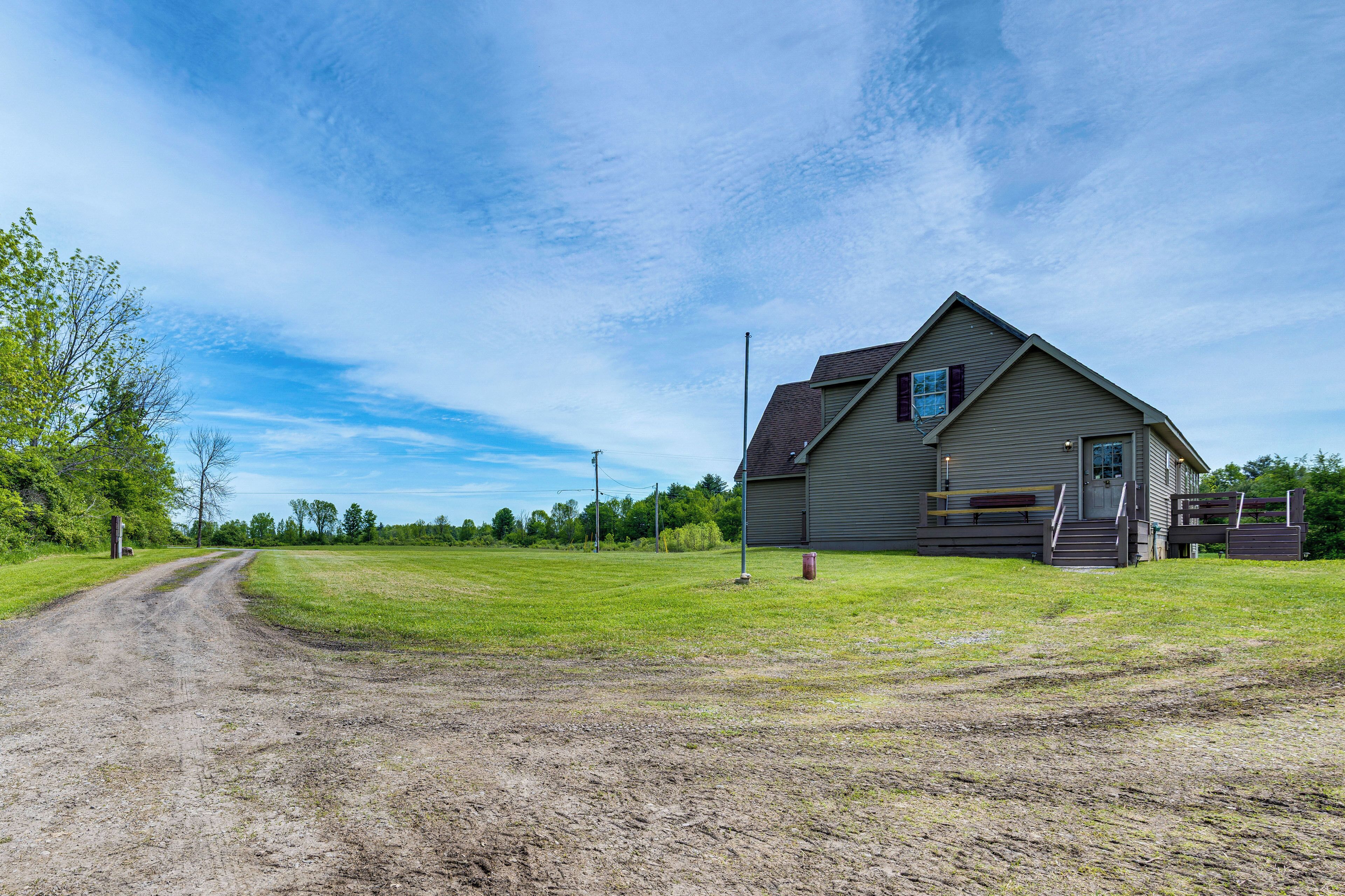 A rural house with a dirt road leading to it, surrounded by green fields and trees.