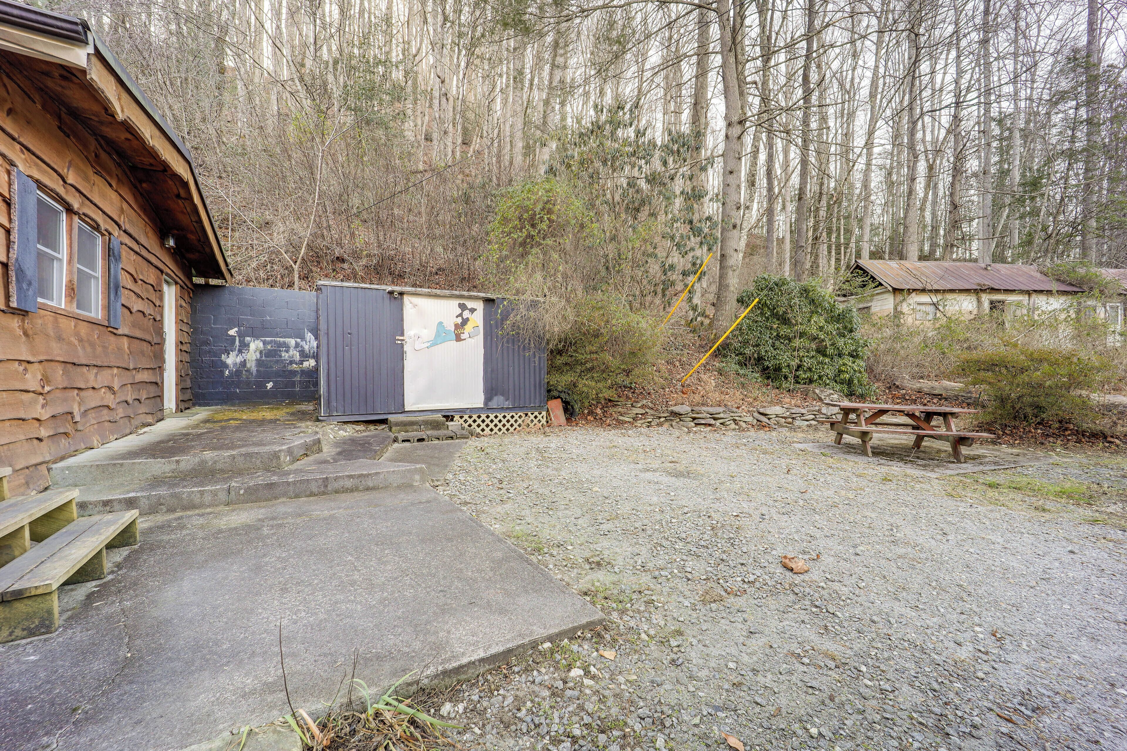 Een rustieke chalet met een betonnen trap naar een houten deur, omgeven door een grindpad en een picknicktafel.