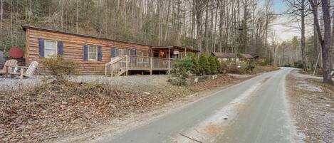 A wooden cabin with a porch and a dirt road leading to it.