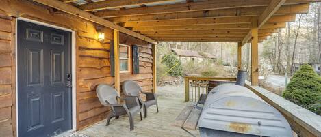 A wooden cabin with a porch, a grill, and two wicker chairs.
