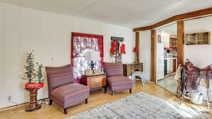 Un salón acogedor con piso de madera, dos sillones estampados, un pequeño árbol de Navidad y una chimenea.