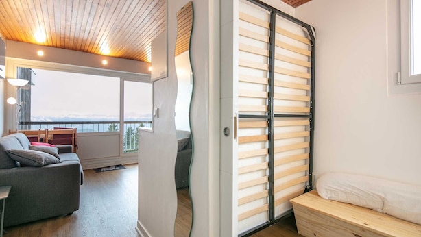 A room with a sliding wooden door, a sofa, a small table, and a view of the outdoors. - Nice Apt for 4 pers near the slopes (Chamrousse)