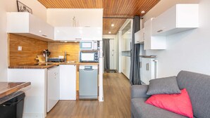A compact kitchenette with a microwave, oven, and dishwasher, a small dining area with a wooden table, and a grey sofa with a red pillow. - Nice Apt for 4 pers near the slopes (Chamrousse)