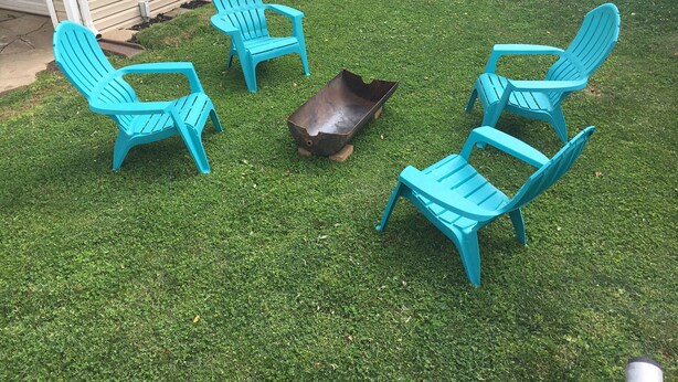 Um quintal com quatro cadeiras Adirondack turquesa dispostas ao redor de um braseiro de metal.