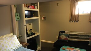 Quarto com cama, escrivaninha, estante, janela com cortinas e sofá.