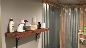 Um banheiro com prateleira de madeira, exibindo produtos de higiene pessoal, uma estatueta de gato branco e um vaso com flores.