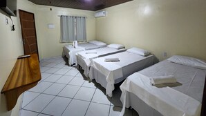A hotel room with three single beds, a wooden desk, a window with curtains, and a tiled floor. - Pousada Nossa Casa Barreirinhas (Barreirinhas)