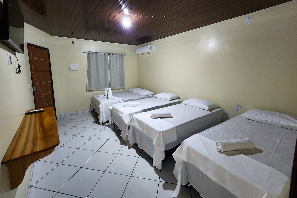 A hotel room with three single beds, a wooden desk, a window with curtains, and a tiled floor.
