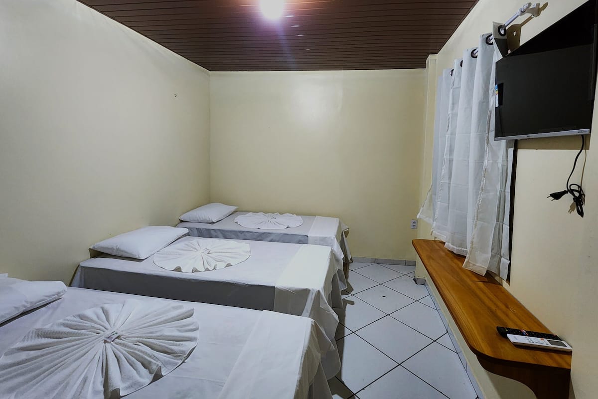 A small, clean room with two beds, a wooden bench, a TV, and a curtain.