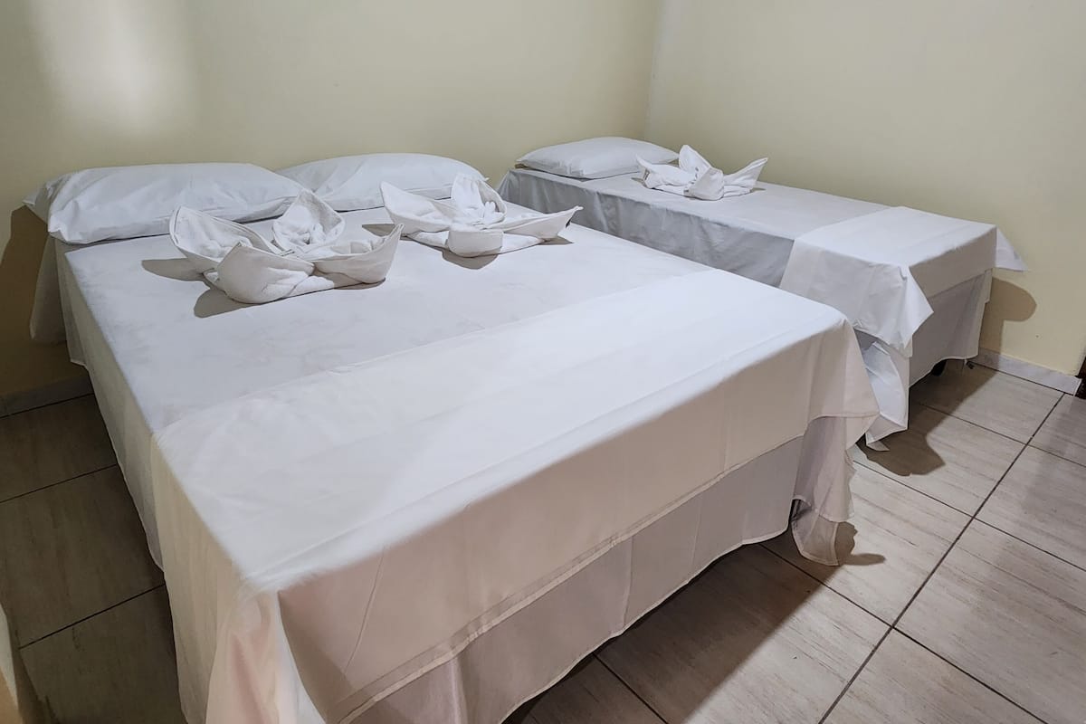 Two single beds with white linens and pillows, a small table with a white tablecloth, and a plain wall.