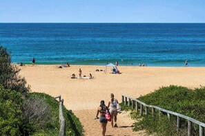 A beach with a wooden walkway leading to the shore, people sunbathing, and a clear view of the ocean.