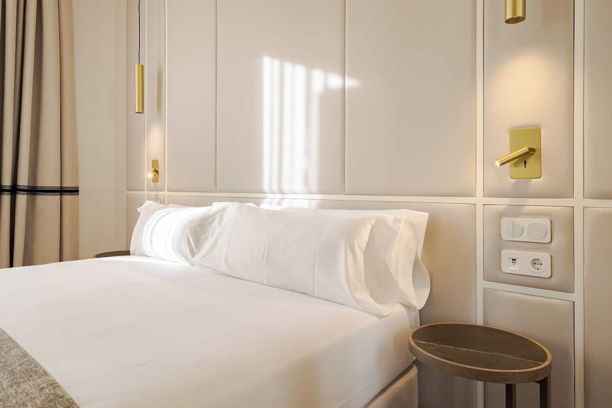 Hotelkamer met een groot bed, nachtkastje, een wandlamp en een stopcontact.
