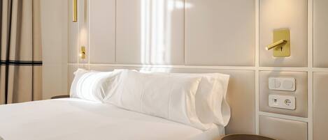 Une chambre d’hôtel avec un grand lit, une table de chevet, une lampe fixée au mur et une prise de courant.