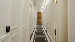 Een hotelgang met witte muren, een zwart-wit gestreept tapijt en een houten deur aan het einde.