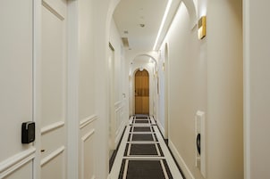 Un corridoio d'hotel con pareti bianche, tappeto a motivi bianco e nero e una porta in legno in fondo.