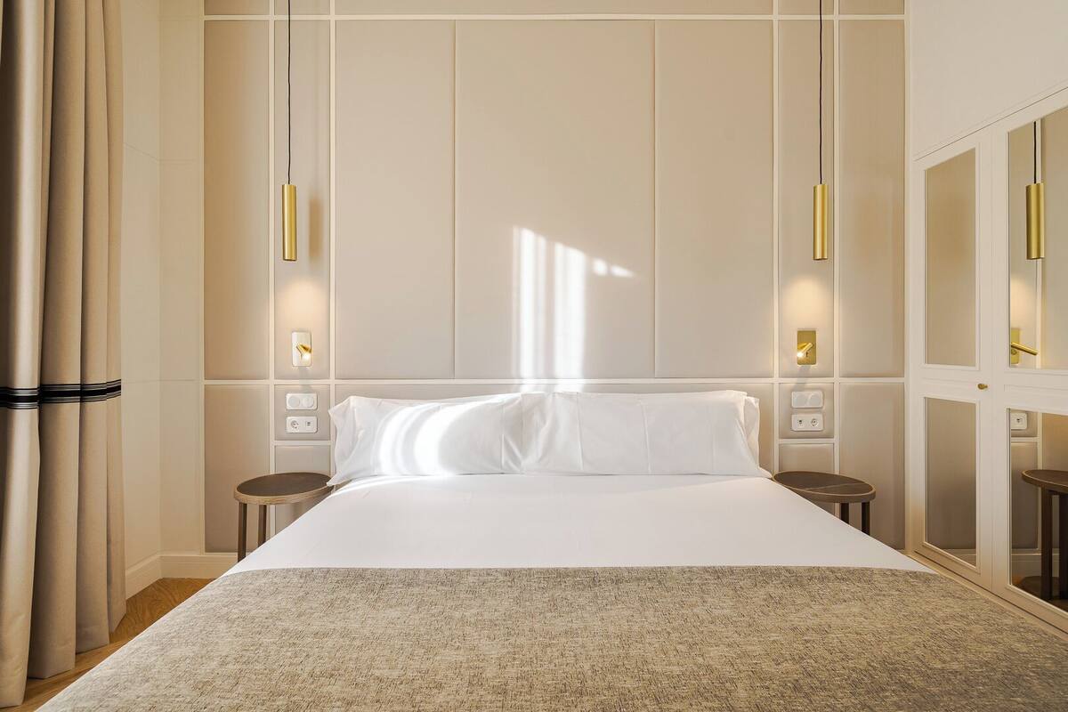 Een hotelkamer met een groot bed, nachtkastjes, een spiegel en wandlampen.