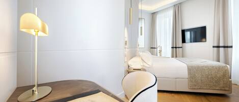 A modern hotel room with a bed, bedside table, lamp, and a flat-screen TV mounted on the wall.