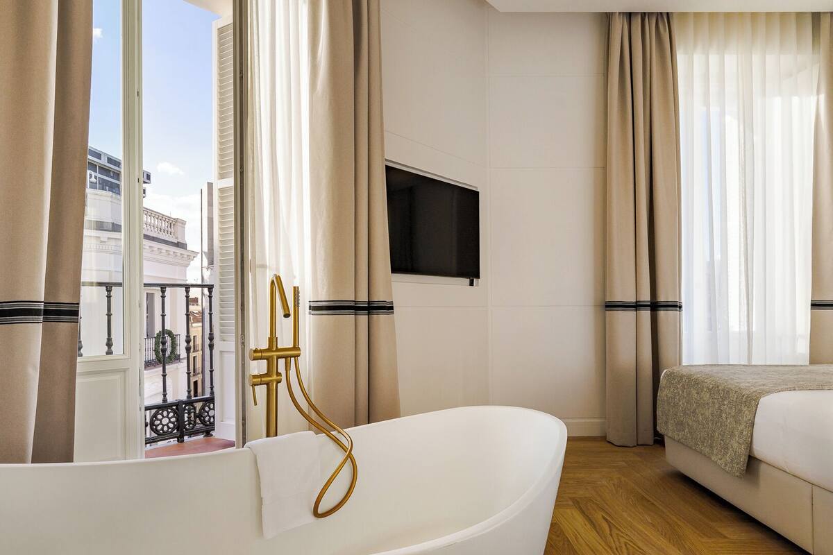 Een moderne hotelkamer met een badkuip, een bed en een aan de muur bevestigde televisie.