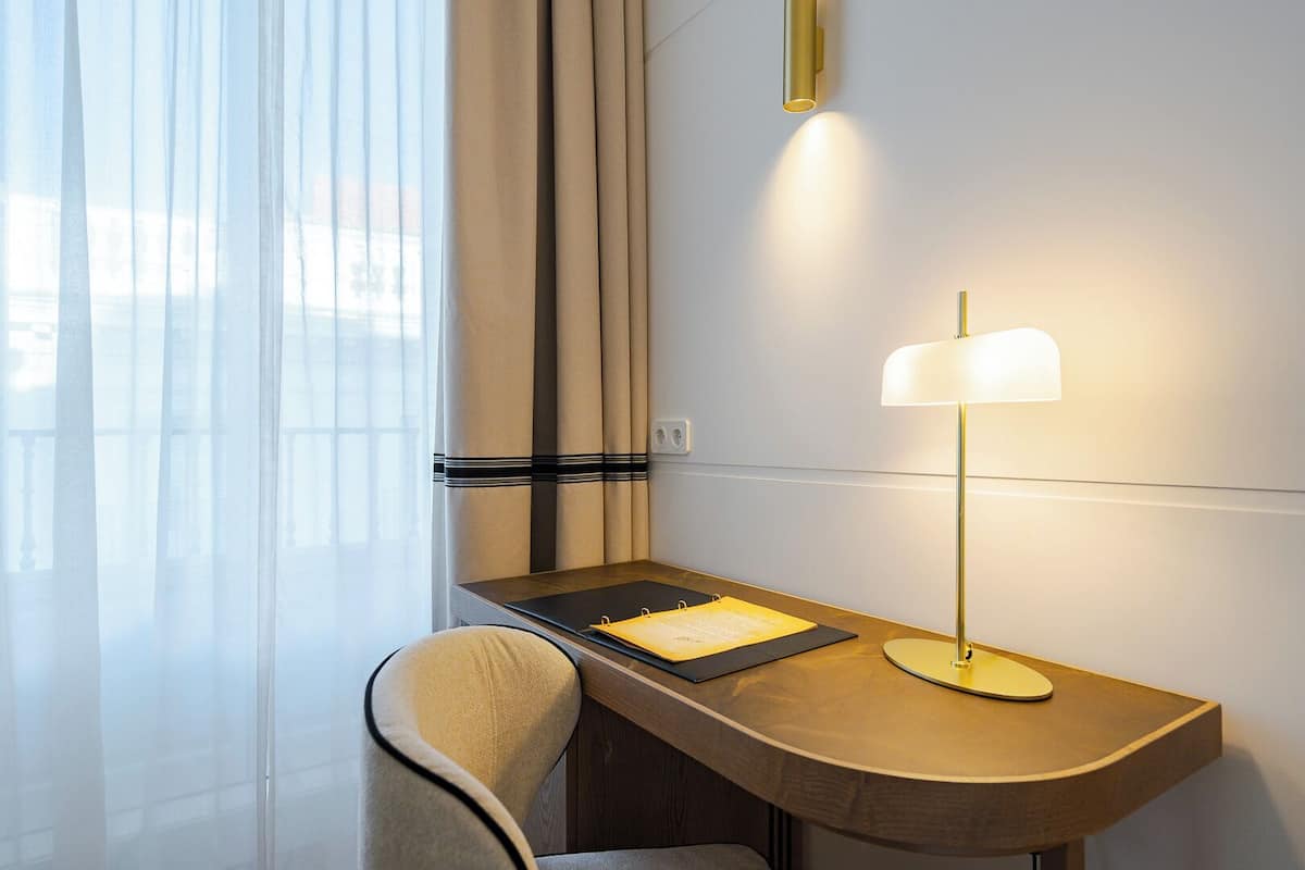 Een hotelkamer met een bureau, een stoel, een lamp en een raam met gordijnen.