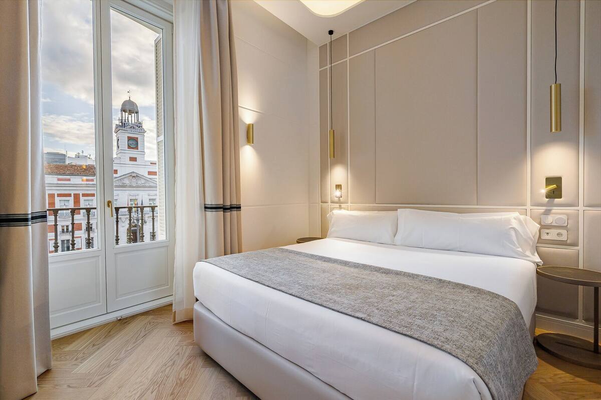Een hotelkamer met een groot bed, uitzicht op een gebouw met een klokkentoren en een raam met gordijnen.