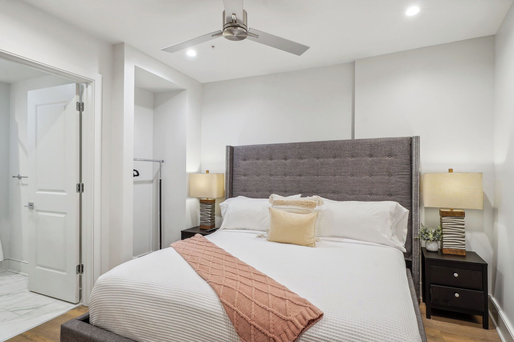 A bedroom with a large bed, two bedside tables, a ceiling fan, and a door to the left.