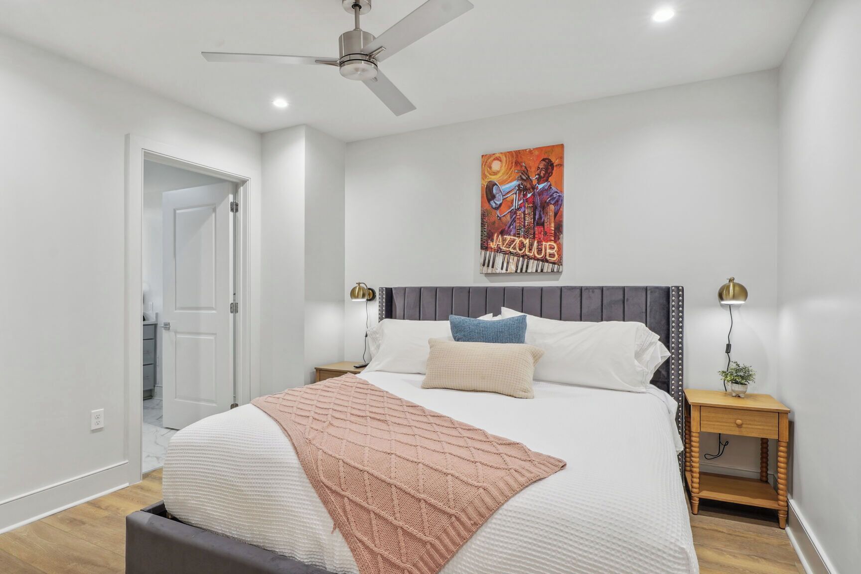 Une chambre à coucher avec un lit, un ventilateur de plafond, un tableau, des lampes de chevet et une petite plante.