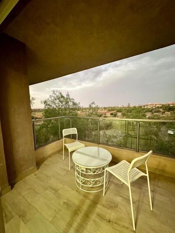 A balcony with a round table and two chairs, overlooking a landscape with trees and buildings.