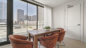 Ein modernes Zimmer mit einem großen Fenster, einem Holztisch, vier gepolsterten Stühlen und einer weißen Tür.