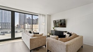 Ein modernes Wohnzimmer mit zwei beigen Sofas, einem flachbildfernseher an der Wand und einem großen Fenster mit Blick auf die Stadt.