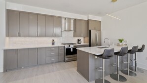 Eine moderne Küche mit grauen Schränken, Edelstahlgeräten und einer zentralen Kochinsel mit Barhocker.