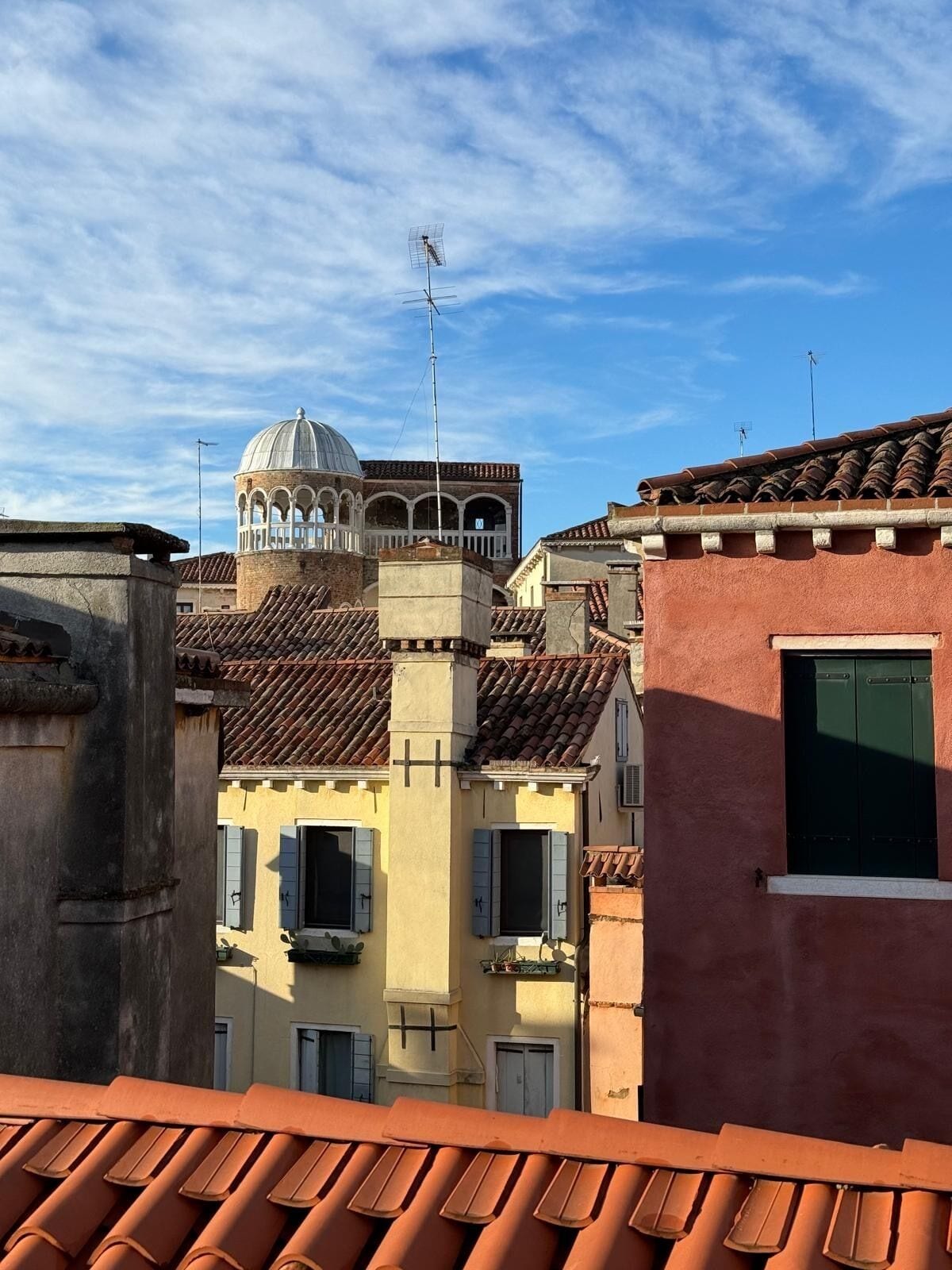 A view of terracotta-tiled rooftops and a historic building with a dome and arches.