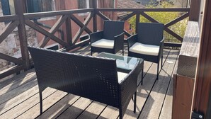 En träaltan med flätade stolar och ett bord i glas.