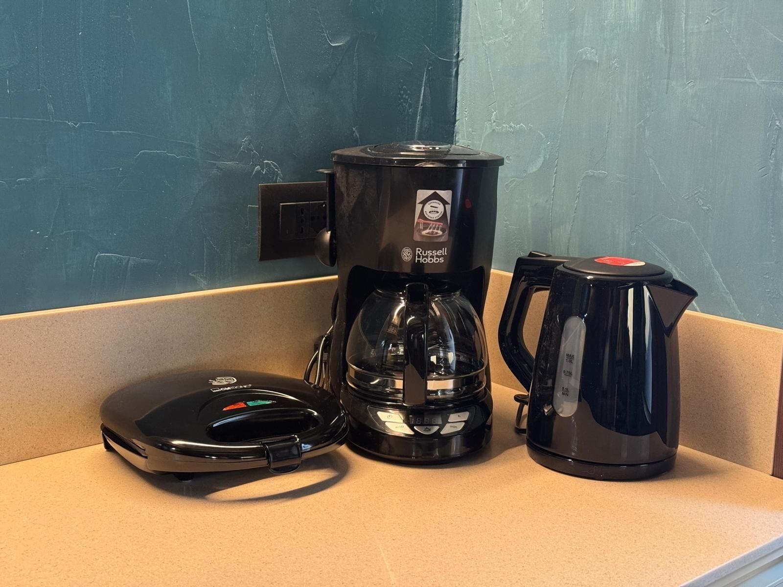 Una cafetera, una jarra de vidrio y una tetera sobre una encimera.