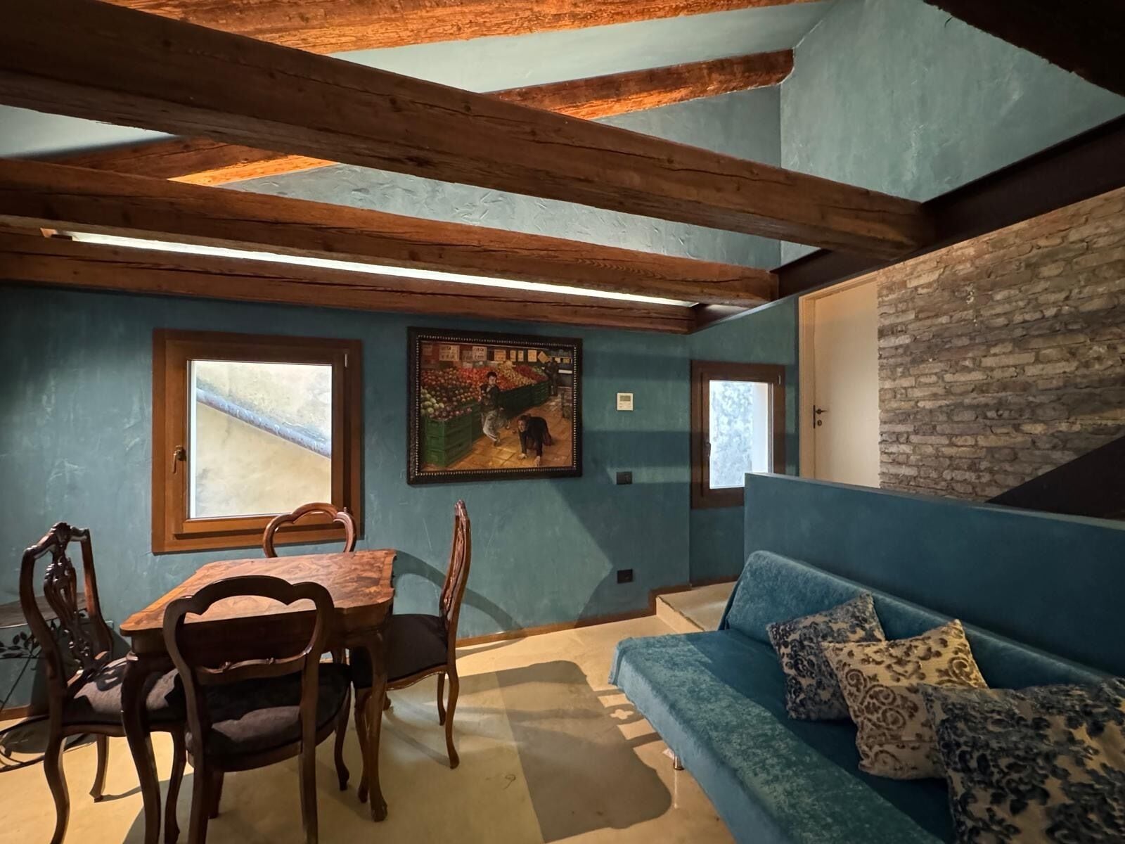 A cozy room with a wooden dining table and chairs, a blue sofa with patterned cushions, and a stone wall.
