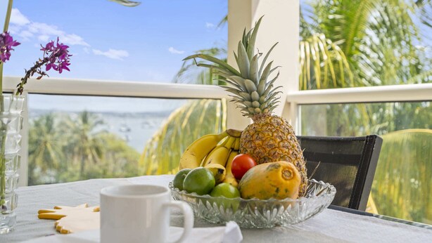 A table with a fruit bowl containing a pineapple, bananas, a tomato, and limes, a white mug, and a vase with flowers. - Villa Harmony - Four Bedroom Villa, Sleeps 10 (Les Trois-Îlets)