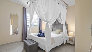 A bedroom with a four-poster canopy bed, a bedside table with a lamp, and a small stool. - Villa Harmony - Four Bedroom Villa, Sleeps 10 (Les Trois-Îlets)