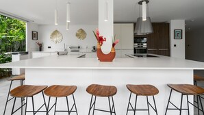 Une cuisine moderne dotée d’un grand îlot central, de tabourets de bar, de luminaires suspendus et d’œuvres d’art décoratives murales.