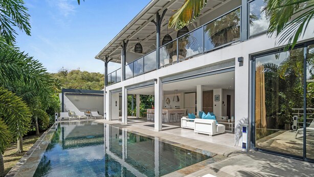 Une maison moderne dotée d’une grande piscine, d’un espace extérieur couvert et d’un balcon offrant une vue sur la piscine.