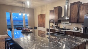 Uma cozinha moderna com uma ilha grande, armários de madeira escura, eletrodomésticos de aço inoxidável e vista através de amplas janelas.