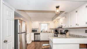 A modern kitchen with white cabinets, stainless steel appliances, a granite countertop, and a wooden floor. - The Terrace Timber House  For 8 (Hamilton)