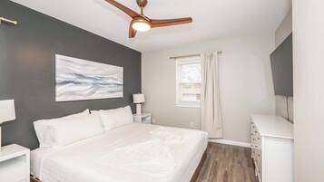 A bedroom with a bed, nightstands, a ceiling fan, a window with curtains, and a painting on the wall.