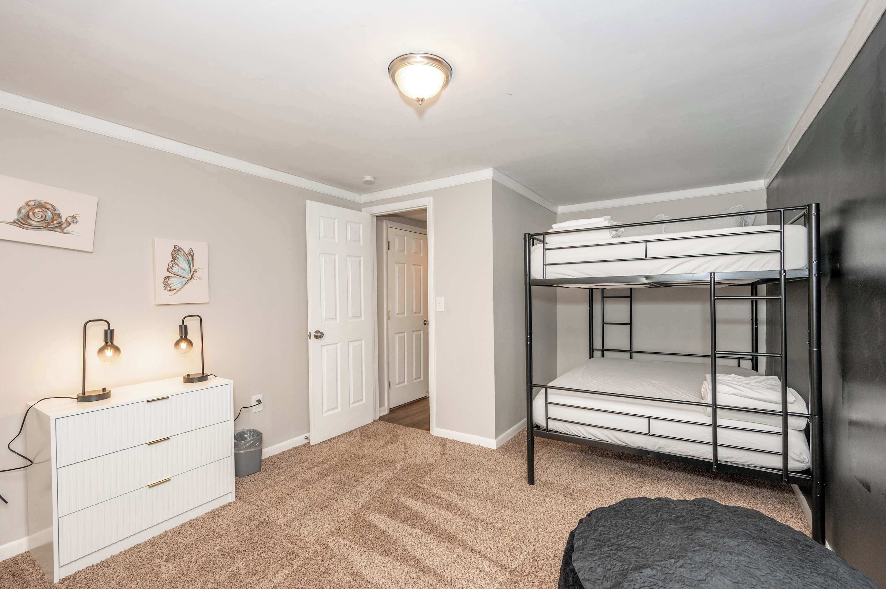 Egy hálószoba emeletes ággyal, két lámpával ellátott komóddal, és egy ajtóval, amely egy másik szobába nyílik.